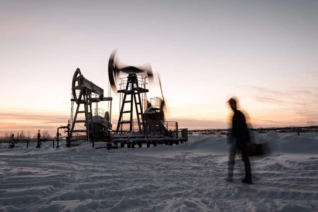 Oil worker in a oilfield. Pump jack and engineer on a winter sunset sky background. Western Siberia. Blurred motion.